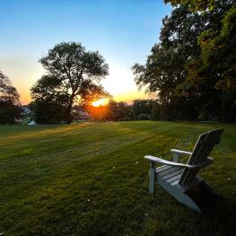 Empty chair in a grass field looking over a sunset.